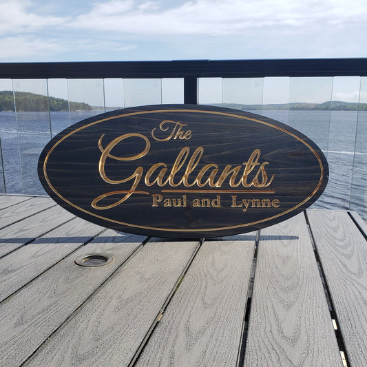 Personalized engraved wood sign 'The Gallants Paul and Lynne' displayed on a wooden deck by water. Custom lake house or coastal welcome sign and couple's gift.