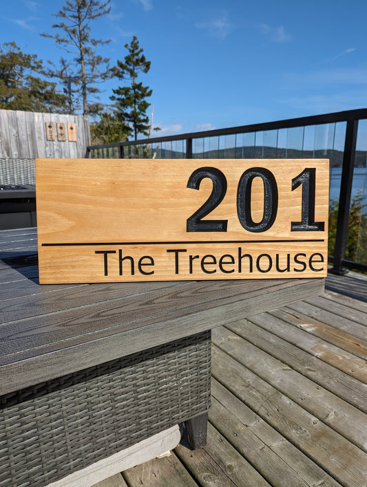 Engraved rectangular wood sign with text '201 The Treehouse'. Custom house number plaque displayed on a deck with outdoor furniture, ideal for unique homes.