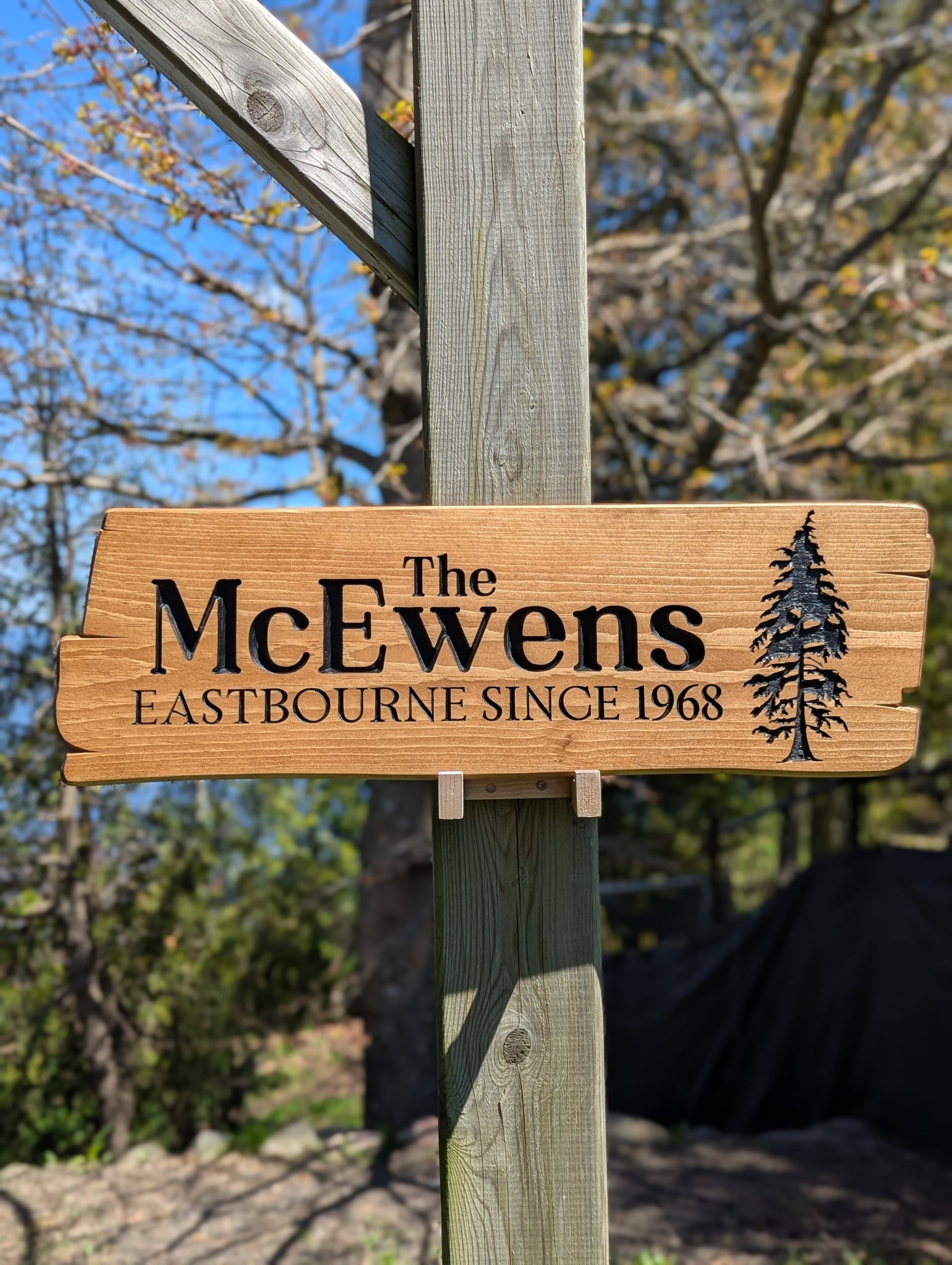 Personalized engraved wood sign with family name, location, and year (Since 1968), featuring rustic tree design. Durable outdoor sign mounted on a post.
