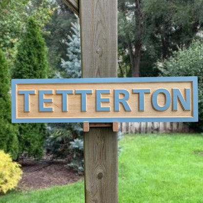 Personalized 'TETTERTON' family name address sign installed in a garden setting. Custom carved wooden home plaque for outdoor display on a house or post.