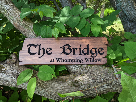 Custom carved wood sign featuring the text 'The Bridge' and 'A Whomping Willow'. Whimsical fantasy rustic sign with hand-carved details, mounted on a tree branch.